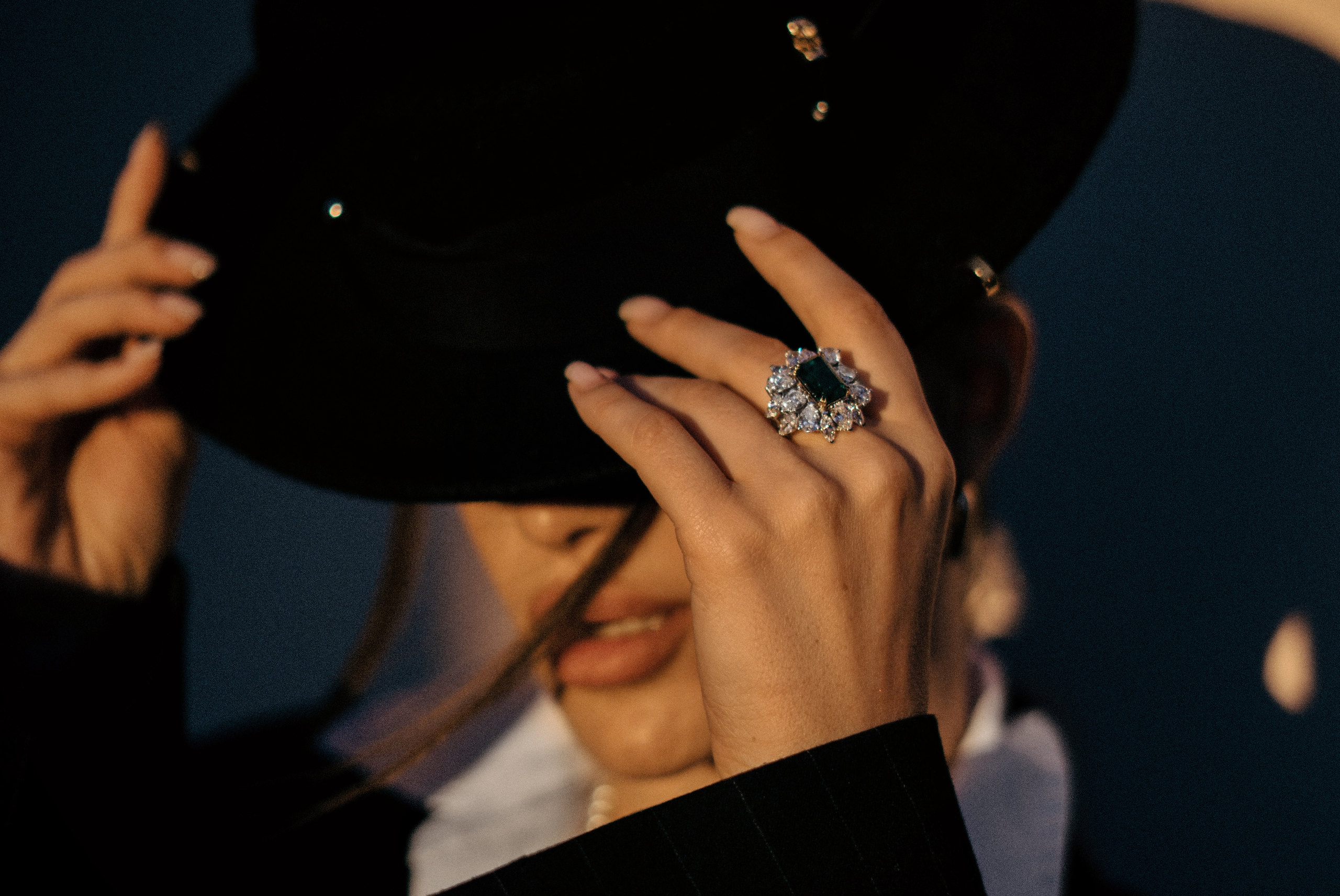 Close-up of a woman in a black hat wearing an emerald and diamond high jewellery ring
