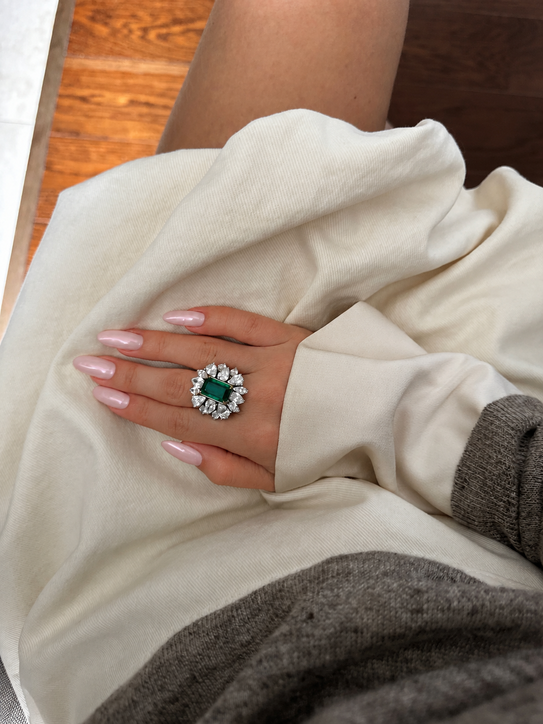 Emerald and diamond ring resting on cream fabric