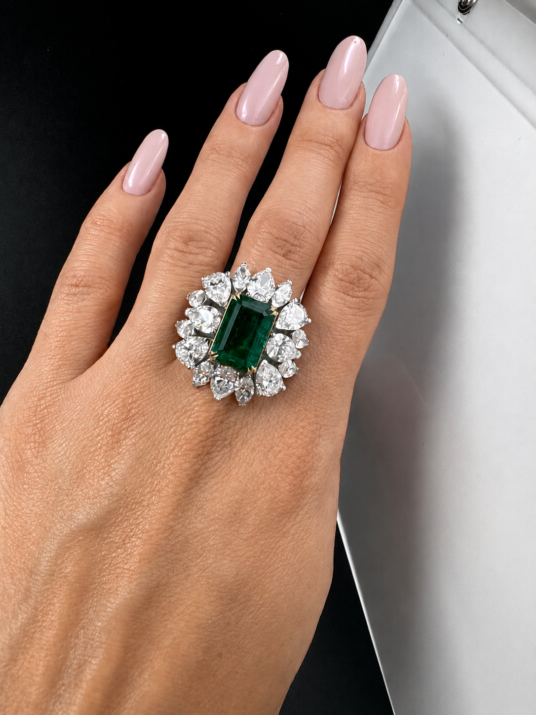 Emerald-cut emerald ring framed with a diamond halo, worn on the hand